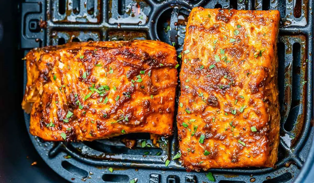 An image capturing the golden-brown Air Fryer Bang Bang Salmon Bites, generously coated in the vibrant Bang Bang sauce, garnished with green onions and sesame seeds, promising a burst of flavor in every bite.