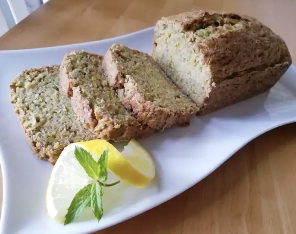 Delicious homemade Lemon Zucchini Bread loaf with lemon slices and fresh zucchinis on a wooden table