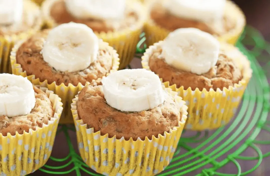A close-up image of freshly baked banana muffins with a moist texture, topped with sliced bananas and a sprinkle of cinnamon.