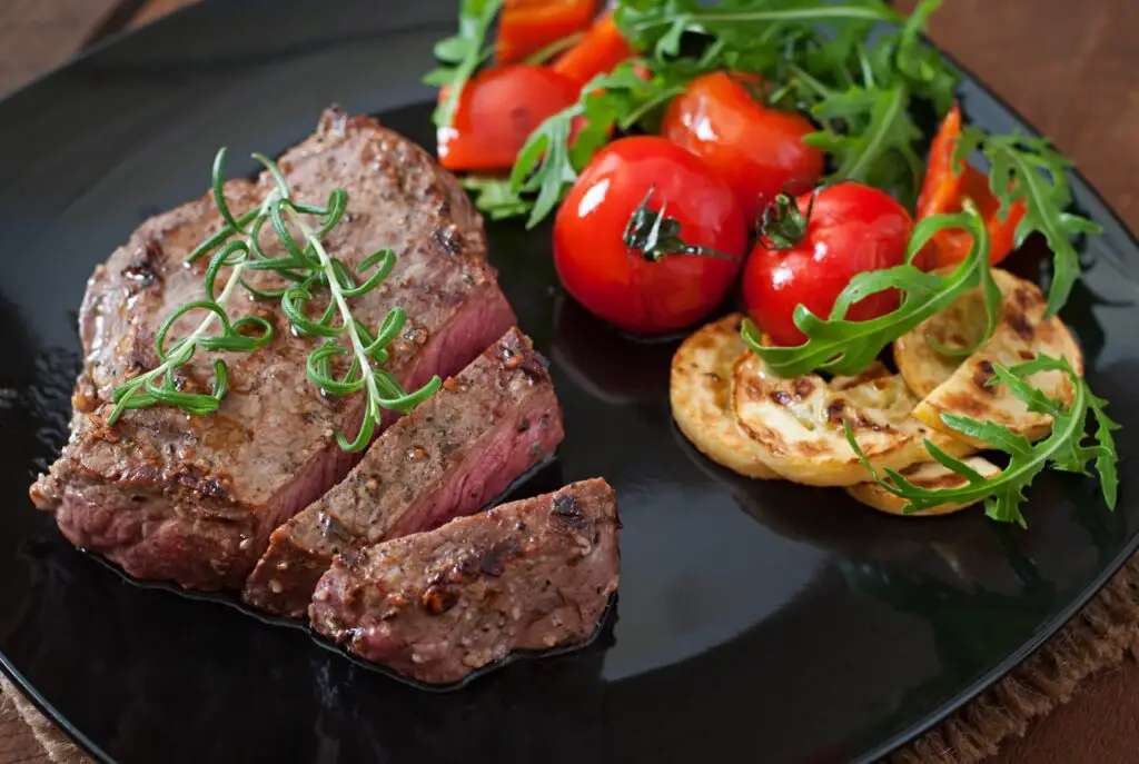 A succulent grilled beef bottom round steak with charred grill marks, served with colorful roasted vegetables.
