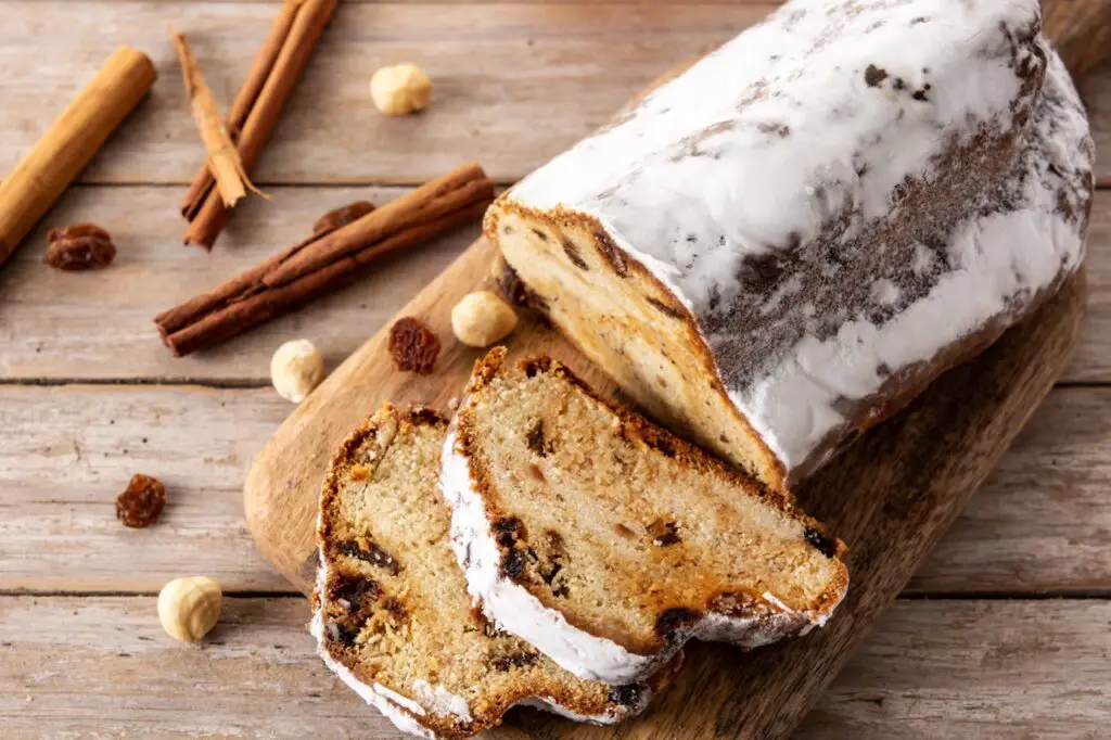 Image of freshly baked Stollen bread, dusted with powdered sugar, surrounded by festive holiday decorations
