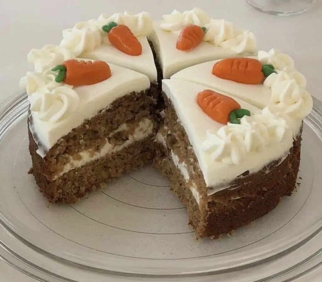 Sliced homemade carrot cake with cream cheese frosting, garnished with chopped nuts and coconut. A delightful treat for any celebration.