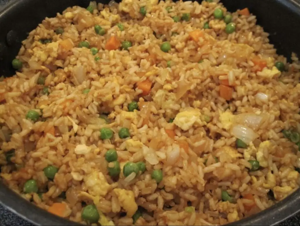 A vibrant image capturing a sizzling wok of Fried Rice—golden grains of jasmine rice, colorful diced vegetables, and scrambled eggs, perfectly seasoned and garnished with green onions. An enticing blend of flavors in every bite.