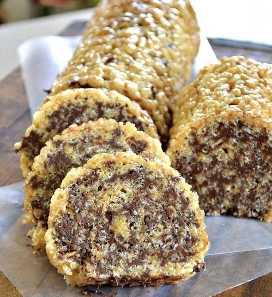 A tempting image capturing the process of rolling up Rice Krispies treats with a luscious peanut butter or Nutella layer, and optional chocolate chips, set against the backdrop of a parchment paper-lined baking sheet. A sweet and playful snack ready to be enjoyed.