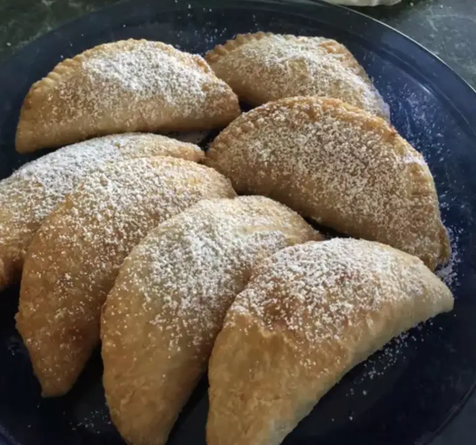 A mouthwatering image showcasing golden-brown Fried Apple and Peach Pies, dusted with powdered sugar and arranged on a plate. The crispy, flaky crust gives way to a warm, spiced fruit filling—a tempting handheld dessert.