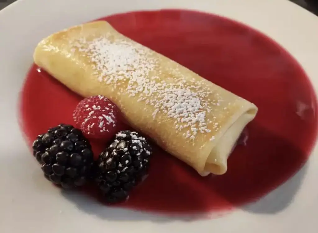 A beautifully plated stack of gluten-free blintzes garnished with fresh berries and a drizzle of honey.