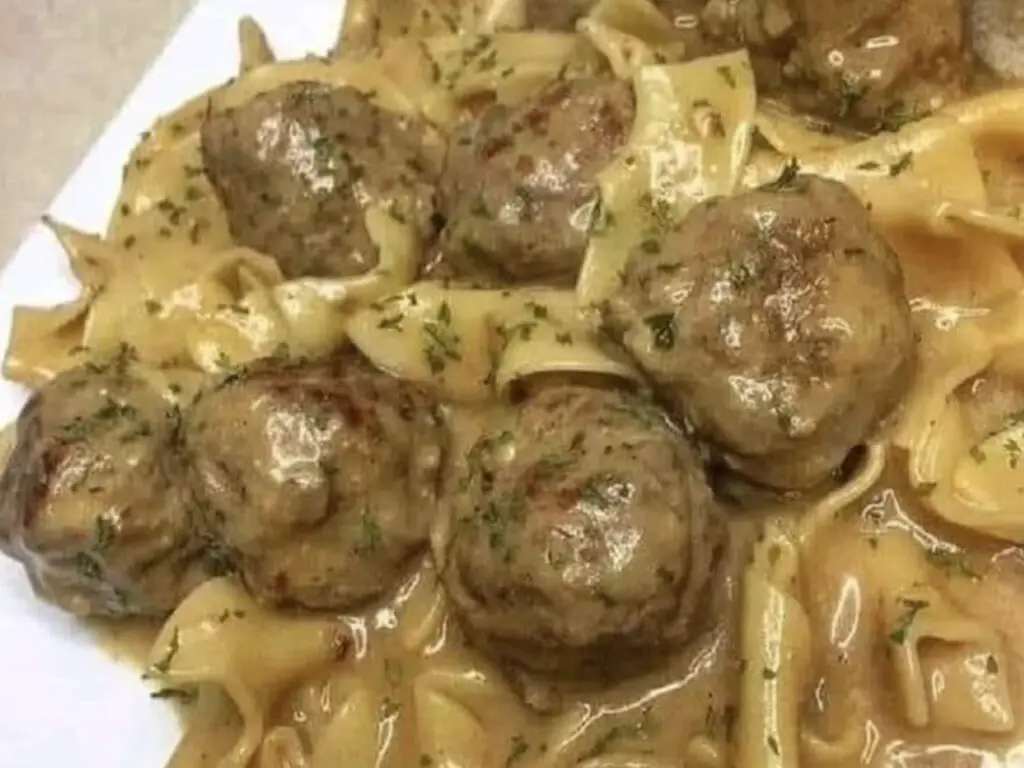 An inviting image featuring a plate of Swedish Meatballs, bathed in a creamy sauce and garnished with fresh herbs. The golden-brown meatballs beckon with their savory aroma, promising a delightful culinary experience.