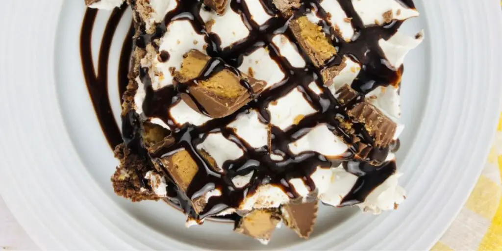A luscious Peanut Butter Cup Dump Cake, featuring layers of chocolate cake mix, peanut butter, chopped peanut butter cups, and a golden-brown topping. Served with whipped cream and garnished with peanut butter cups.