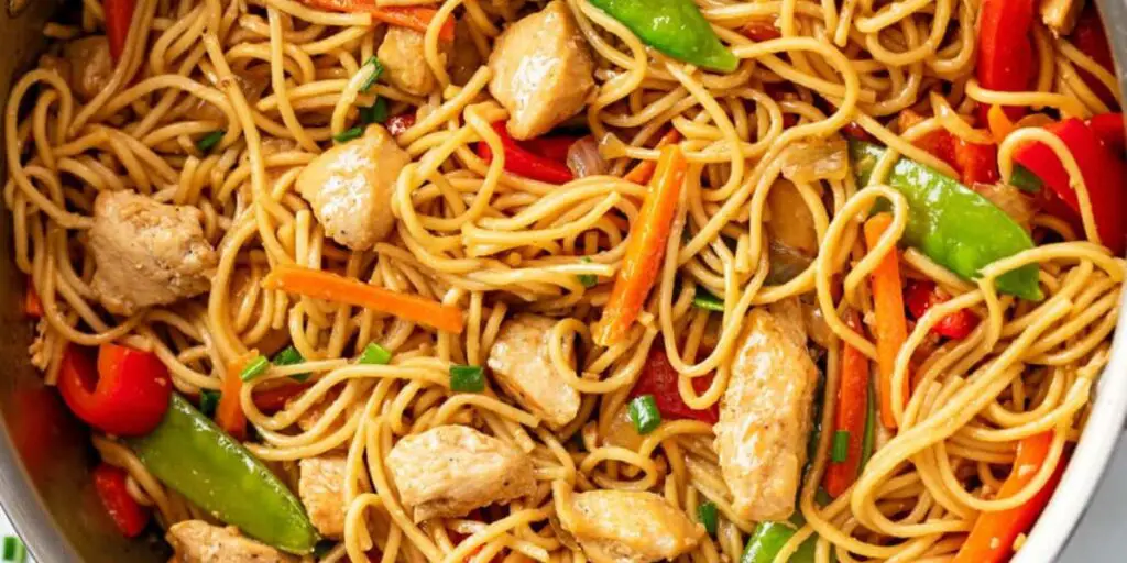 A vibrant plate of Chicken Lo Mein, featuring tender sliced chicken, lo mein noodles, and an array of colorful vegetables, garnished with sesame seeds. A feast for the eyes and taste buds!