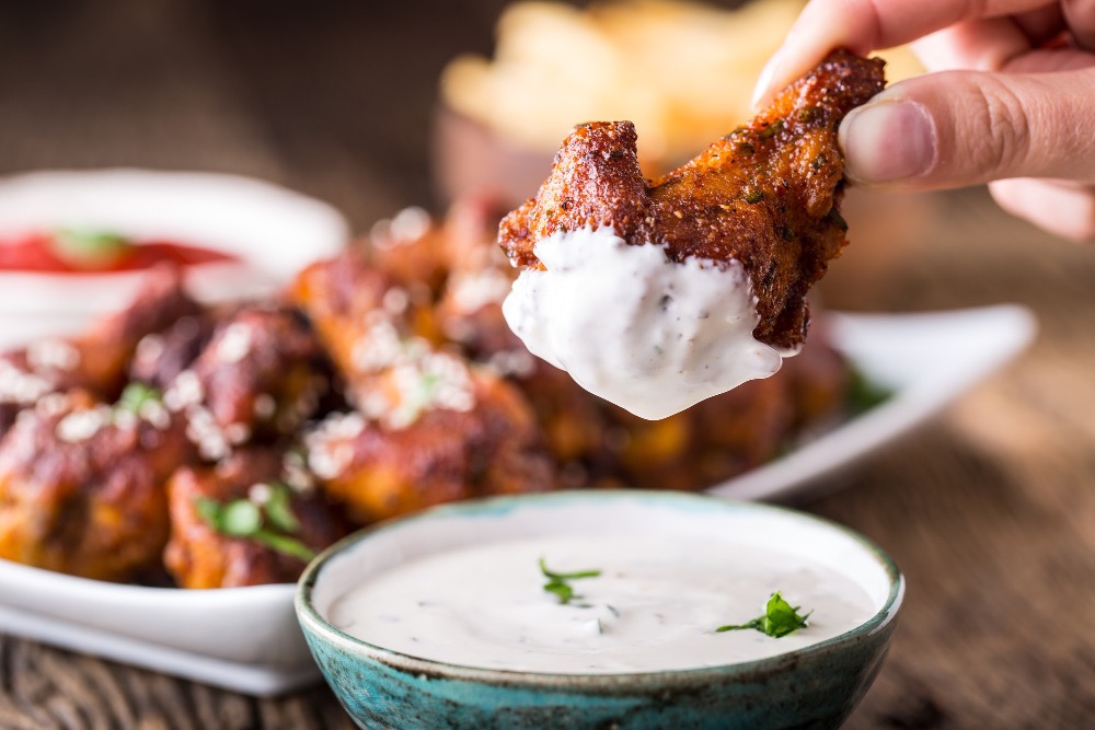 A bowl of Wingstop's famous ranch sauce, with a backdrop of crispy chicken wings.
