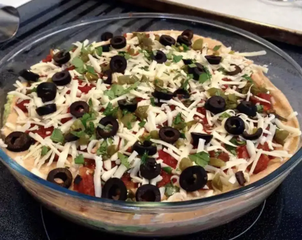 An image showcasing a beautifully layered Taco Dip, with vibrant colors and fresh toppings, ready to be scooped up with tortilla chips.